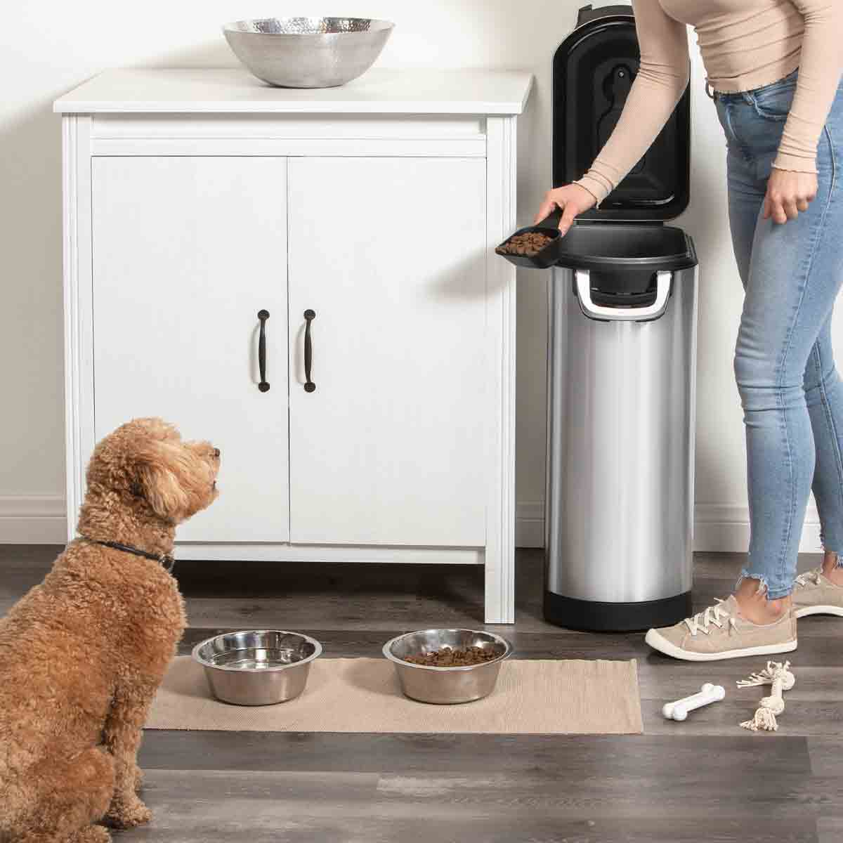 Lifestyle view of Simplehuman X-Large Pet Food Can, Brushed Stainless Steel, open for easy scooping while feeding a dog.